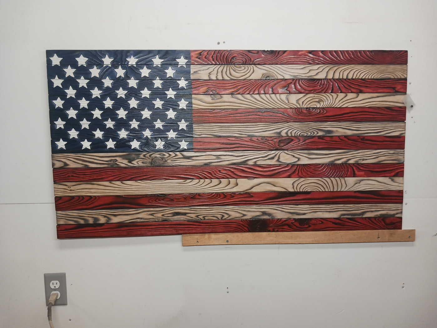 A rustic wooden American flag encased in a wooden frame, highlighting its artisanal design and national pride